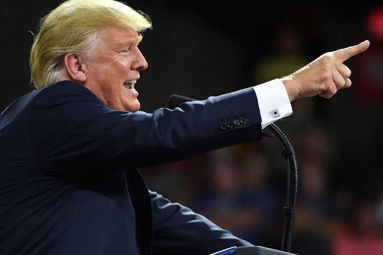 President Trump points while speaking from a podium during a political rally.